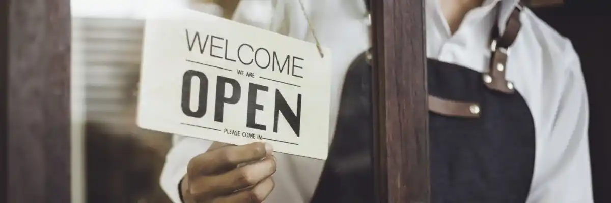 Small business owner flips Welcome We Are Open sign