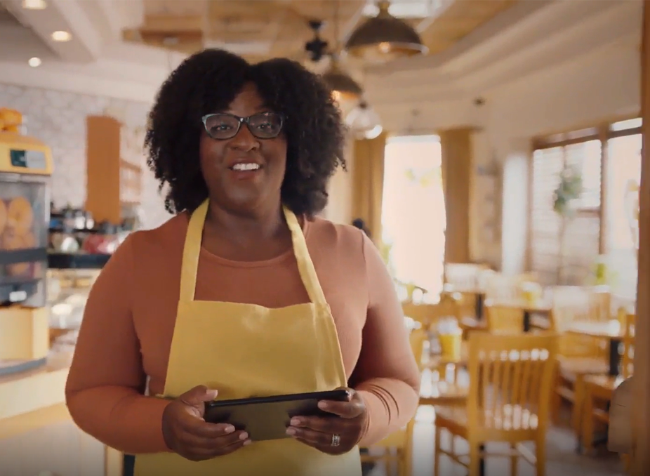Woman holding device with cafe in background.