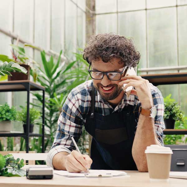 man-curly-hair-glasses-working-on-phone-writing-notes-plants